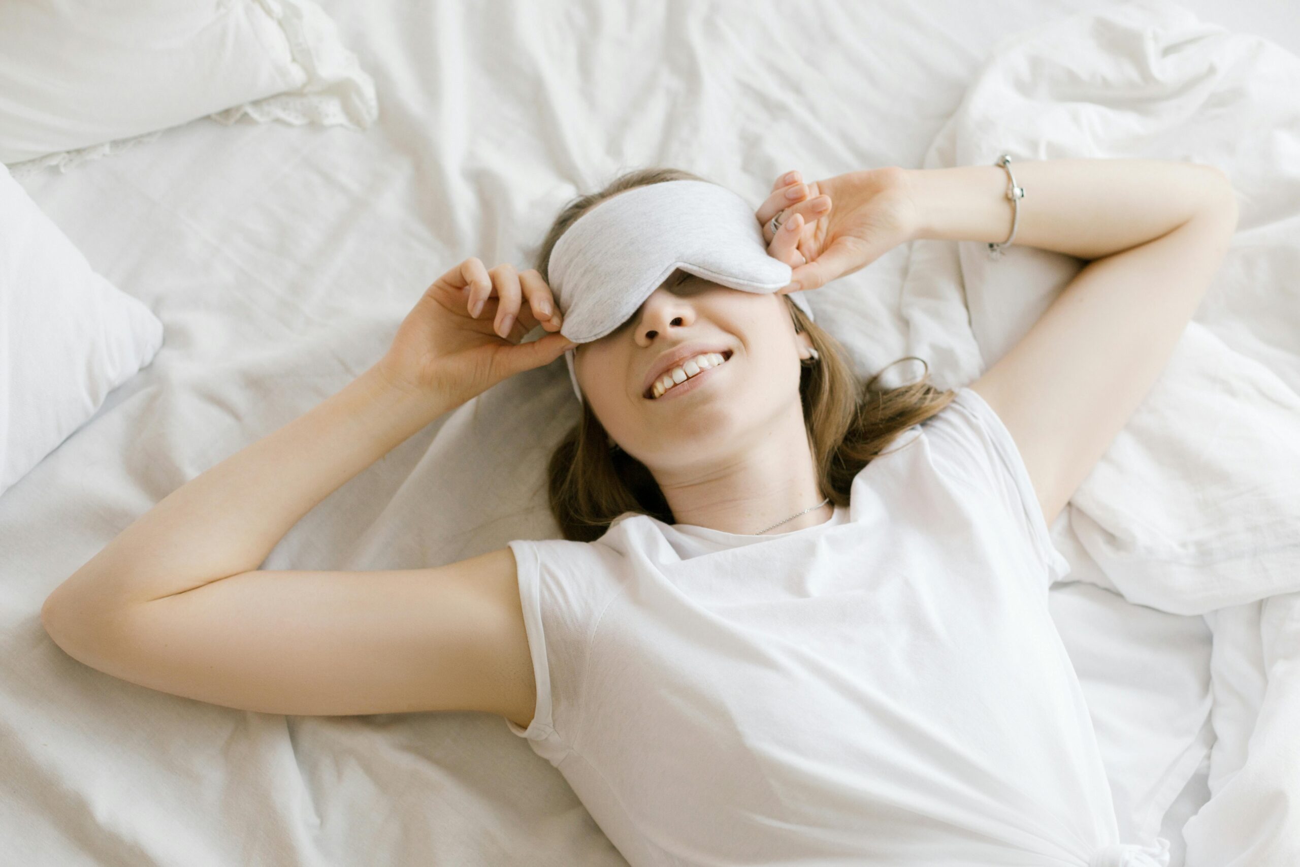 A serene young woman enjoying relaxation with a sleep mask in her cozy bed.